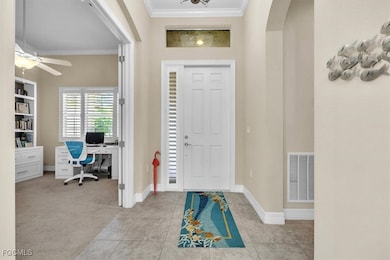 Entrance foyer featuring crown molding, light tile patterned floors, light carpet, arched walkways, and a ceiling fan