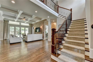Staircase featuring a ceiling fan, ornamental molding, wood finished floors, ornate columns, and beamed ceiling