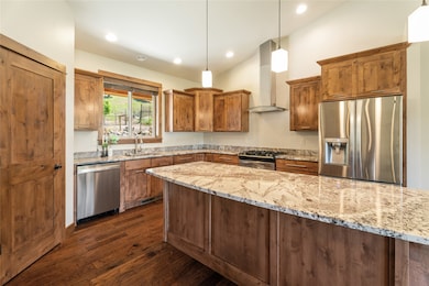 Kitchen with stainless steel appliances, wall chimney range hood, dark wood-style flooring, light stone countertops, and recessed lighting