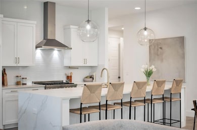Kitchen featuring a kitchen breakfast bar, wall chimney exhaust hood, white cabinetry, decorative backsplash, and decorative light fixtures