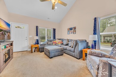 Carpeted living area with high vaulted ceiling, plenty of natural light, and a ceiling fan