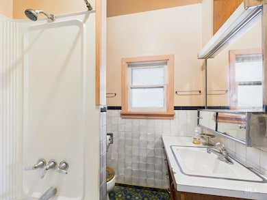 Full bathroom with vanity, tile walls, wainscoting, tub / shower combination, and tile patterned flooring