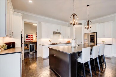 Kitchen with appliances with stainless steel finishes, beverage cooler, under cabinet range hood, a chandelier, and a kitchen island with sink