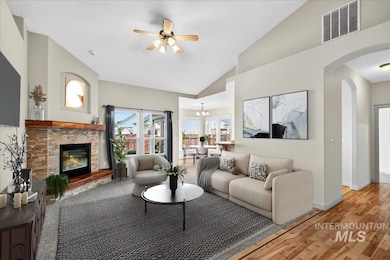 Living room with wood finished floors, arched walkways, a glass covered fireplace, a ceiling fan, and a chandelier
