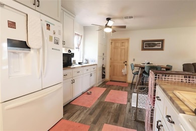 Kitchen with white fridge with ice dispenser, white cabinets, dark wood finished floors, a ceiling fan, and black microwave