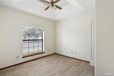 Empty room featuring a raised ceiling, baseboards, light wood finished floors, and ceiling fan