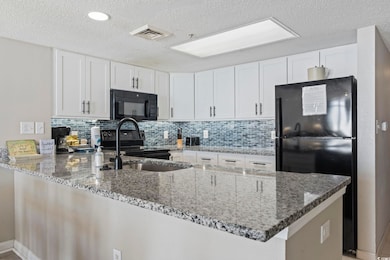 Kitchen featuring a peninsula, black appliances, dark stone countertops, white cabinetry, and a textured ceiling