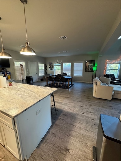 Kitchen with open floor plan, hanging light fixtures, dark wood-style floors, and light stone countertops