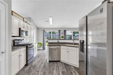 Kitchen with appliances with stainless steel finishes, a textured ceiling, white cabinetry, wood finished floors, and dark countertops