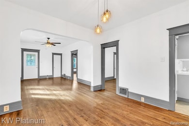 Unfurnished living room featuring arched walkways, light wood-style flooring, ornamental molding, and a ceiling fan