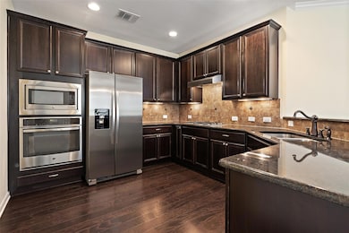 Kitchen featuring dark brown cabinetry, stainless steel appliances, decorative backsplash, dark wood finished floors, and dark stone countertops