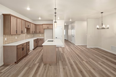 Kitchen featuring an island with sink, backsplash, a chandelier, decorative light fixtures, and recessed lighting