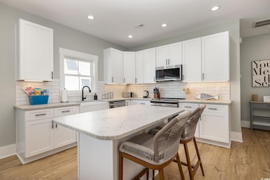 Kitchen with a kitchen bar, light stone countertops, white cabinets, light wood-style floors, and recessed lighting