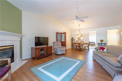 Living room with wood finished floors, ceiling fan, a fireplace, a chandelier, and high vaulted ceiling