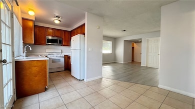 Kitchen with light countertops, light tile patterned floors, white appliances, a textured ceiling, and brown cabinets