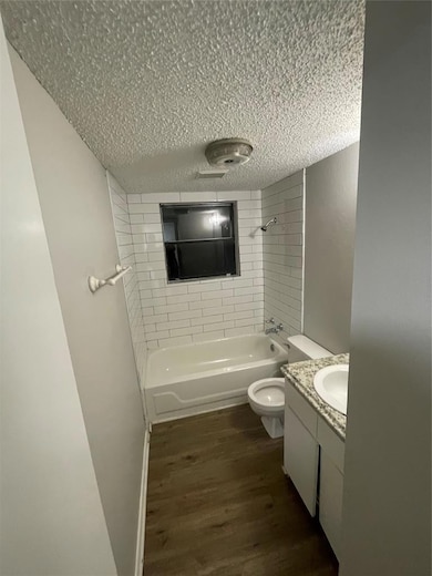 Bathroom with vanity, bathtub / shower combination, dark wood finished floors, and a textured ceiling