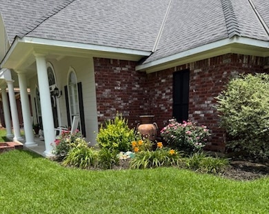 View of property exterior featuring brick siding, a lawn, a shingled roof, and covered porch