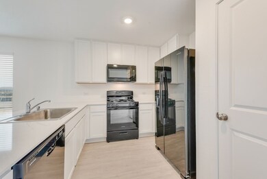 Kitchen with light wood-style flooring, a sink, white cabinetry, light countertops, and black appliances