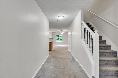 Hall with light carpet, a textured ceiling, and stairs