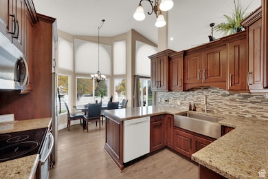 Kitchen featuring a chandelier, decorative light fixtures, appliances with stainless steel finishes, light stone counters, and light wood-style flooring