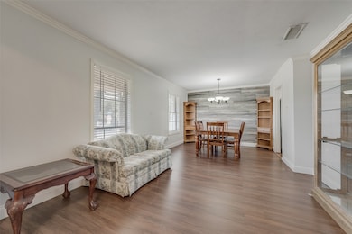 Living area with wood finished floors, a chandelier, ornamental molding, and an accent wall