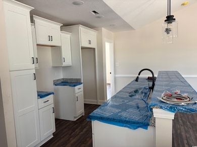Kitchen with white cabinets, dark wood-style flooring, hanging light fixtures, a textured ceiling, and dark stone countertops