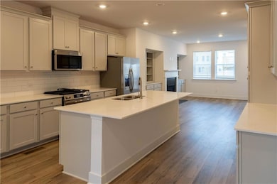 Kitchen with tasteful backsplash, light stone countertops, appliances with stainless steel finishes, dark wood-style flooring, and a center island with sink