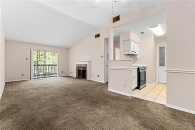 Unfurnished living room featuring light colored carpet, vaulted ceiling, ceiling fan, a fireplace with flush hearth, and light tile patterned flooring