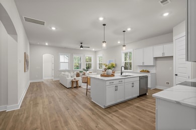Kitchen featuring a ceiling fan, arched walkways, a center island with sink, recessed lighting, and light stone counters