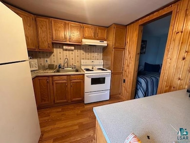 Kitchen featuring white appliances, a sink, under cabinet range hood, light wood-type flooring, and brown cabinetry