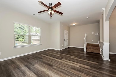 Spare room featuring dark wood-style floors, a ceiling fan, and stairway
