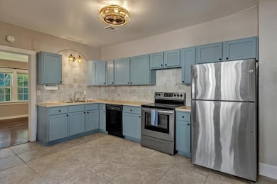 Kitchen with stainless steel appliances, blue cabinetry, light countertops, and tasteful backsplash