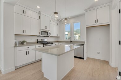Kitchen with stainless steel appliances, pendant lighting, a center island, white cabinetry, and recessed lighting