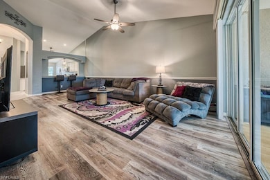 Living area featuring light wood-style flooring, a ceiling fan, arched walkways, and high vaulted ceiling