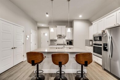 Kitchen featuring tasteful backsplash, white cabinetry, stainless steel appliances, and decorative light fixtures