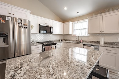 Kitchen featuring appliances with stainless steel finishes, white cabinetry, light stone counters, vaulted ceiling, and backsplash