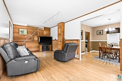 Living area with wooden walls, a chandelier, rail lighting, light wood-style flooring, and a wainscoted wall