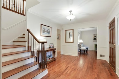 Entrance foyer with stairway, wood finished floors, and ornamental molding