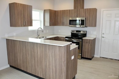Kitchen with stainless steel appliances, a peninsula, modern cabinets, brown cabinetry, and light wood-type flooring