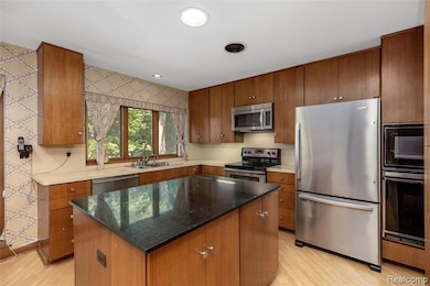 Kitchen featuring appliances with stainless steel finishes, a kitchen island, dark stone counters, recessed lighting, and brown cabinets