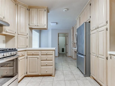 Kitchen with stainless steel appliances, a peninsula, light tile patterned floors, under cabinet range hood, and light countertops