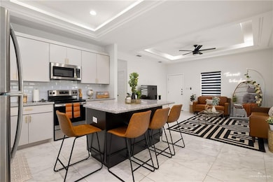 Kitchen featuring a tray ceiling, appliances with stainless steel finishes, backsplash, and white cabinetry