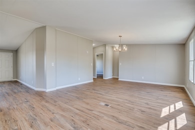 Unfurnished room featuring light wood-type flooring, a chandelier, and vaulted ceiling