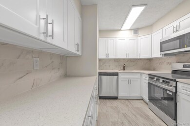 Kitchen featuring stainless steel appliances, white cabinets, tasteful backsplash, light stone countertops, and a textured ceiling