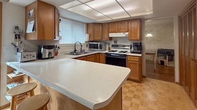 Kitchen featuring brown cabinets, light countertops, range with gas cooktop, a peninsula, and stainless steel microwave