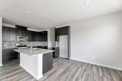 Kitchen with light hardwood / wood-style flooring, backsplash, light stone countertops, an island with sink, and appliances with stainless steel finishes