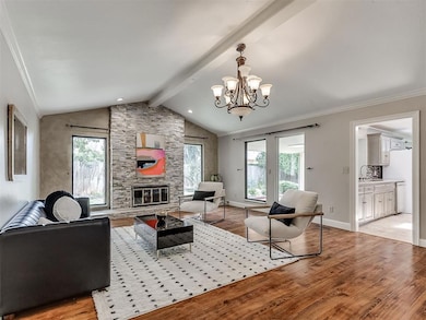 Living room featuring light wood-style flooring, a stone fireplace, a chandelier, and ornamental molding