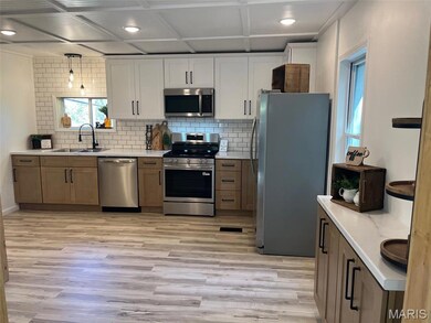 Kitchen featuring appliances with stainless steel finishes, brown cabinetry, white cabinets, tasteful backsplash, and pendant lighting