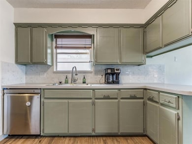 Kitchen with stainless steel dishwasher, light countertops, decorative backsplash, light wood-type flooring, and green cabinets