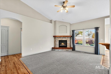 Unfurnished living room with vaulted ceiling, light wood-style flooring, a fireplace, arched walkways, and a ceiling fan
